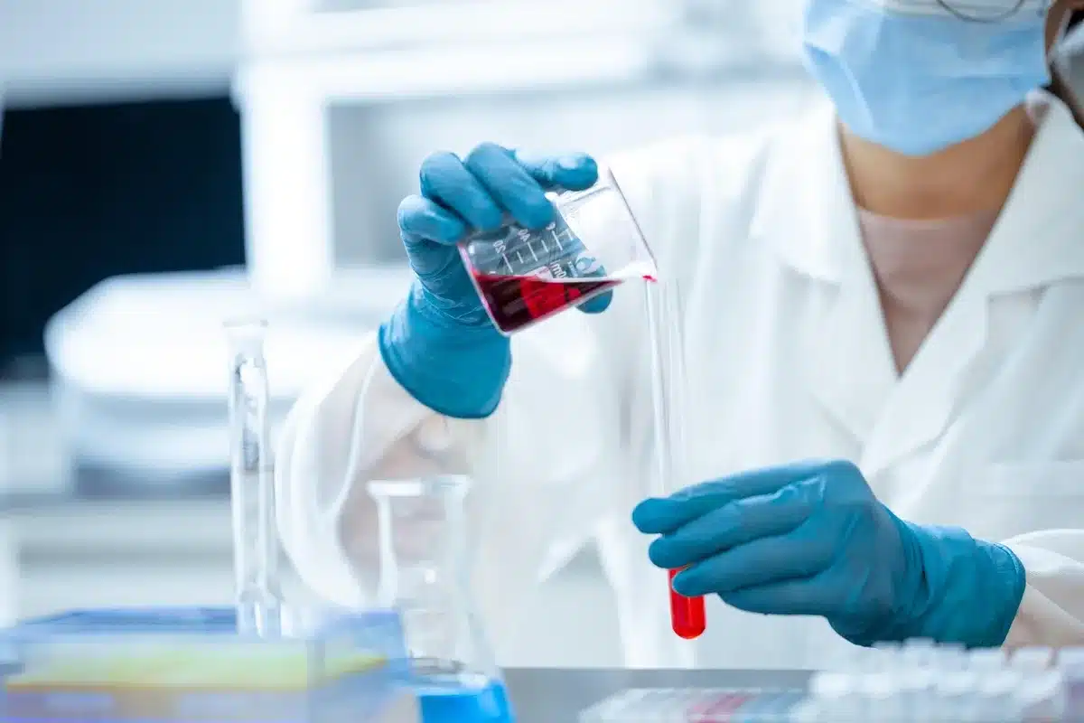 Researcher holding an amphibian specimen in a laboratory setting with scientific equipment blurred in the background.