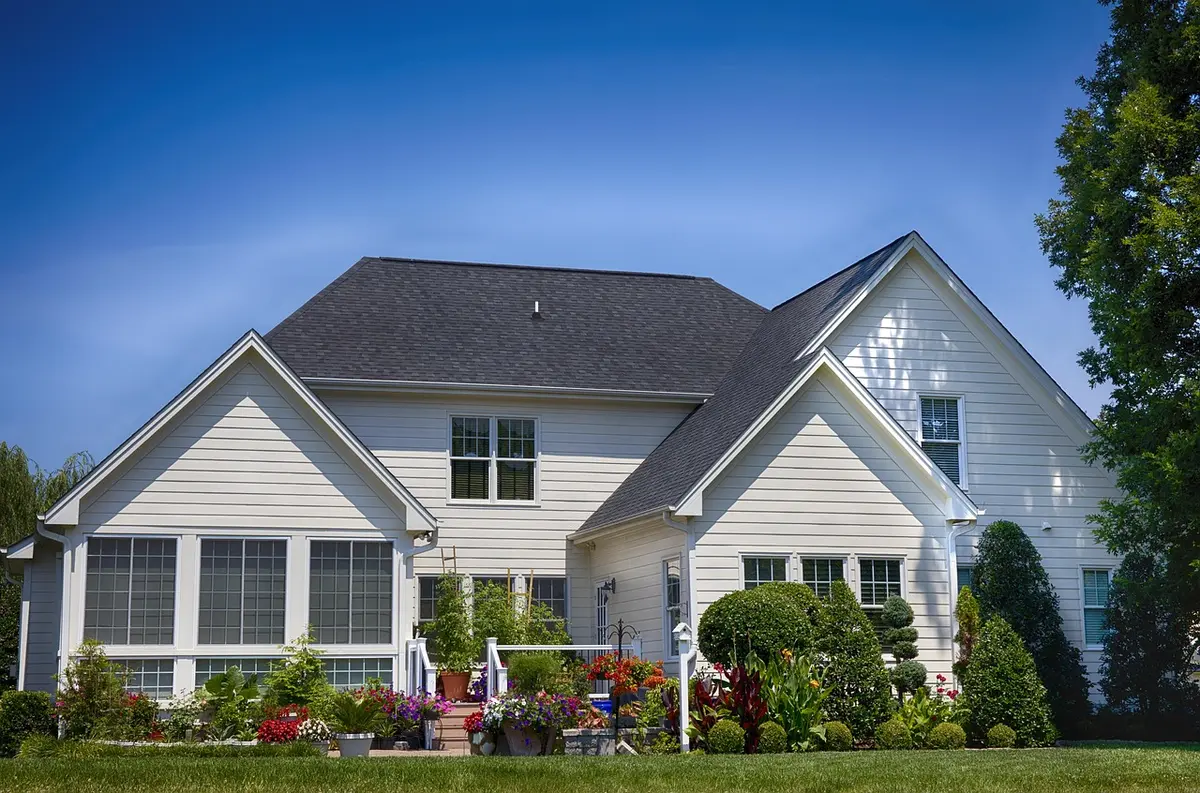 A person holds a house key in front of a modest suburban home with a small garden