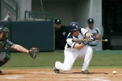 Hands placing a baseball and a blue cap on a dugout bench, blurred teammates behind