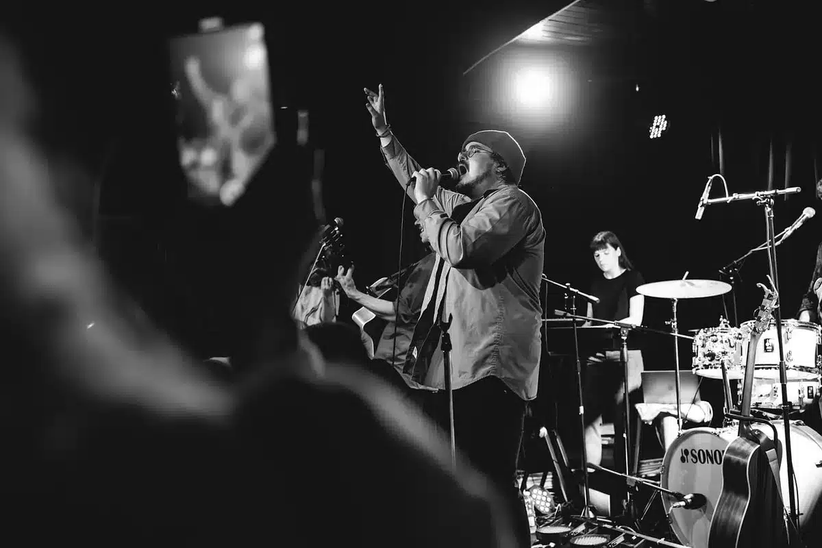 Silhouette of a performer onstage with fans and raised signs in the crowd