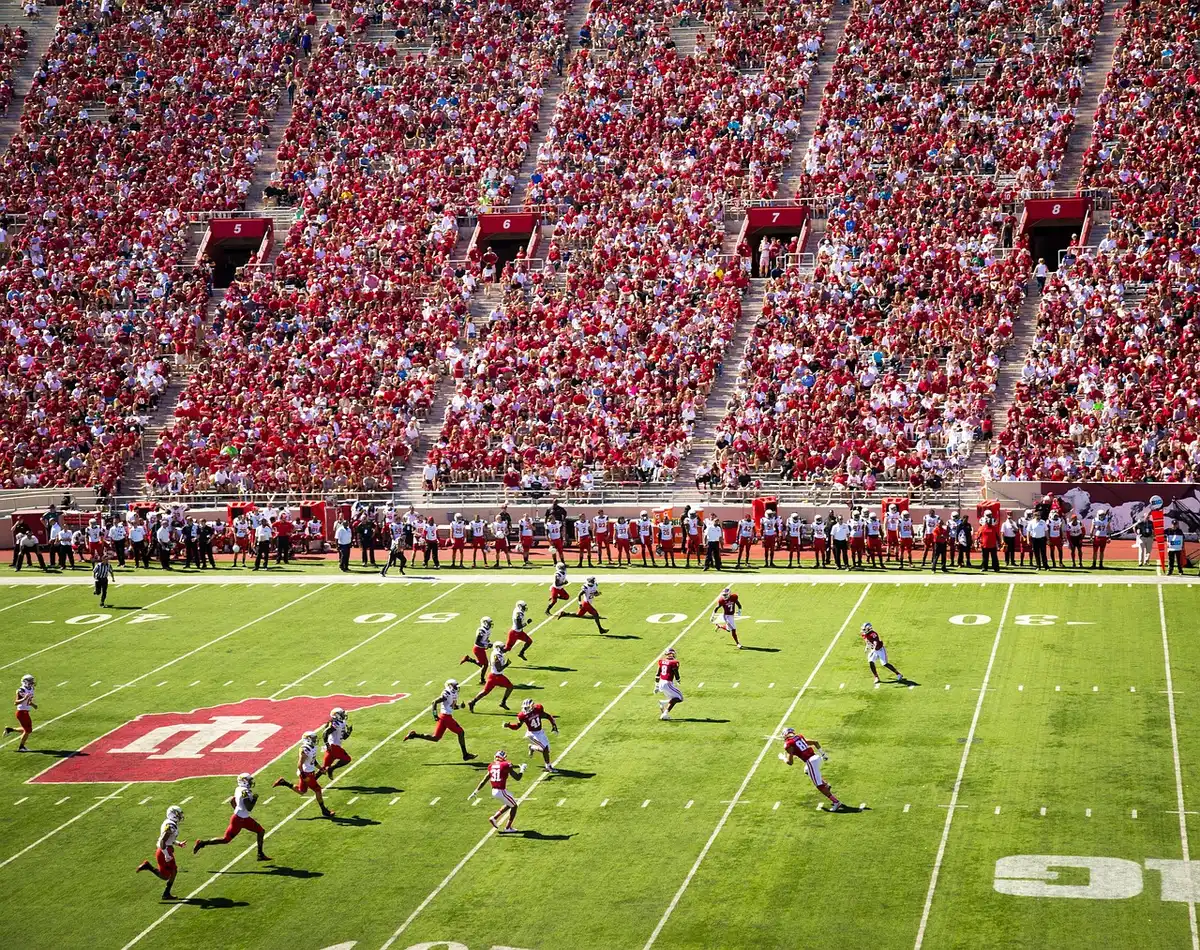 Silhouette of a receiver leaping for a catch near a defender on a college football sideline