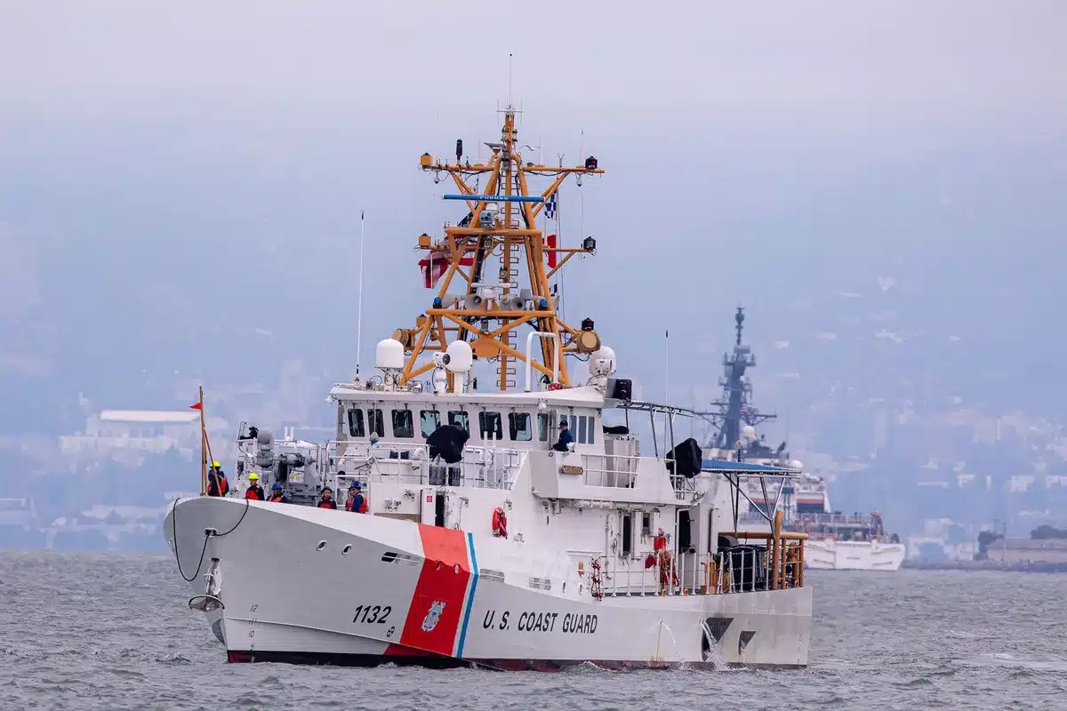 Rescue vessel approaching a crowded inflatable boat off a rocky coast