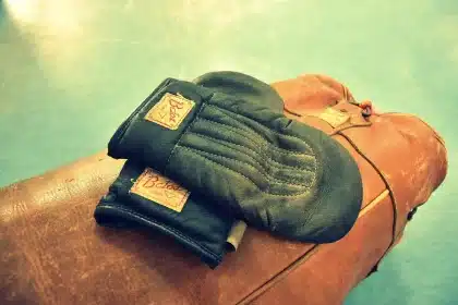 Worn punching bag and taped gloves in a training gym, evoking combat sports finance debate
