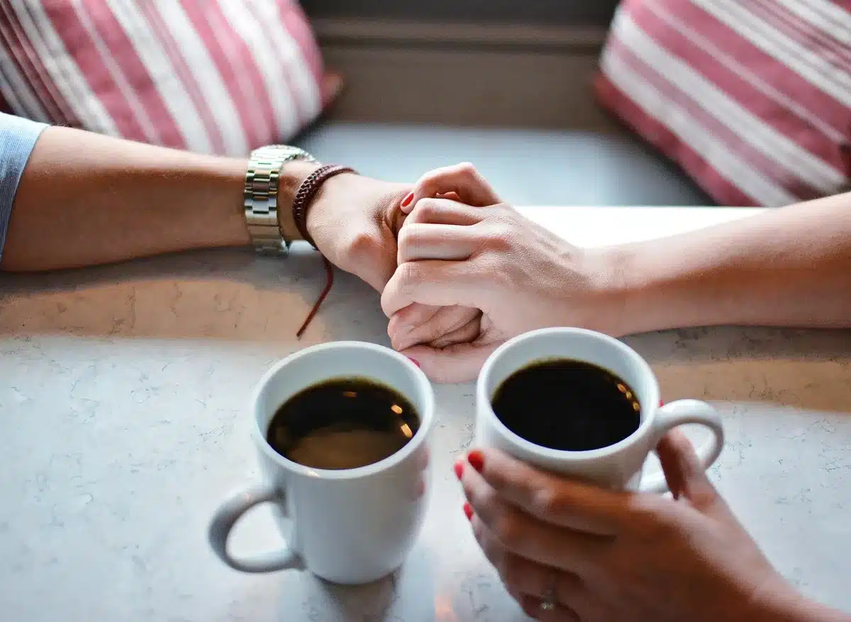 Two coffee cups, a notebook and anonymous hands holding a pen on a café table